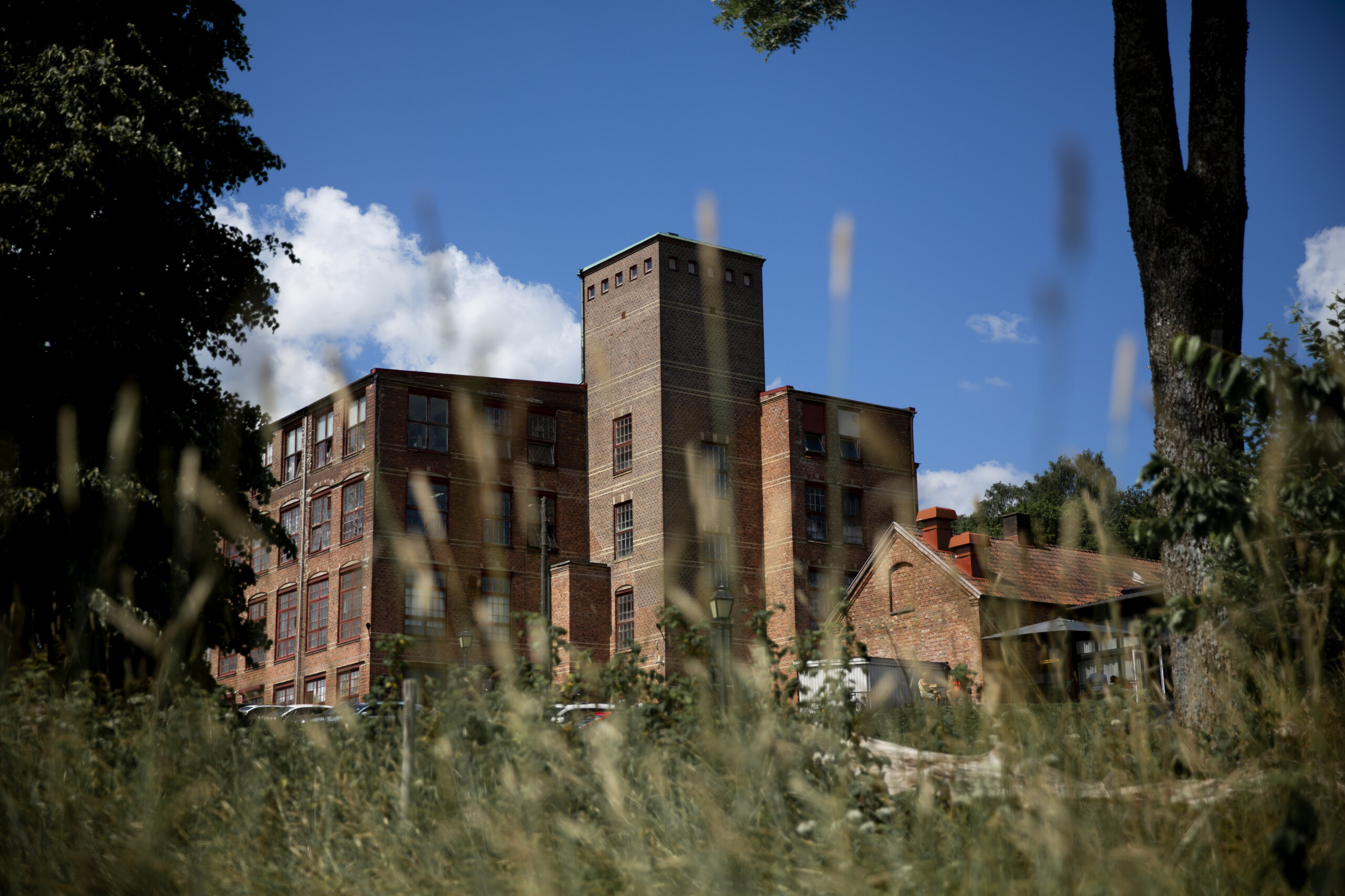 Exteriör med grönska i förgrunden av Spinneriet i Lindome.